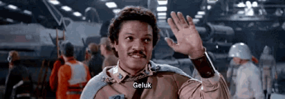 a man with a mustache is waving his hand and the word geluk is on his chest