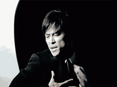 a man in a black suit and tie is holding his hands to his chest