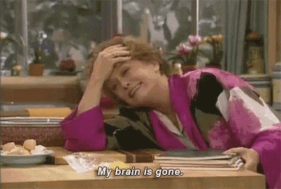 a woman is sitting at a table with her hand on her forehead and saying `` my brain is gone . ''
