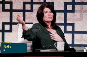 a woman is sitting at a desk with a cup of coffee and a sign that says karen .