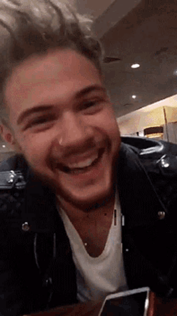 a man with a nose ring is smiling while sitting at a table with a cell phone