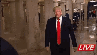 a man in a suit and red tie is standing in a hallway with soldiers .
