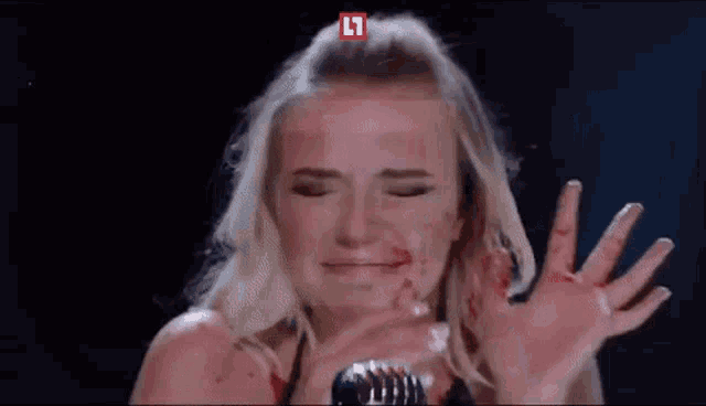 a woman with blood on her face is singing into a microphone on a stage .
