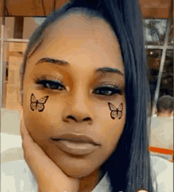 a woman with butterflies on her face is holding her hand to her chin .