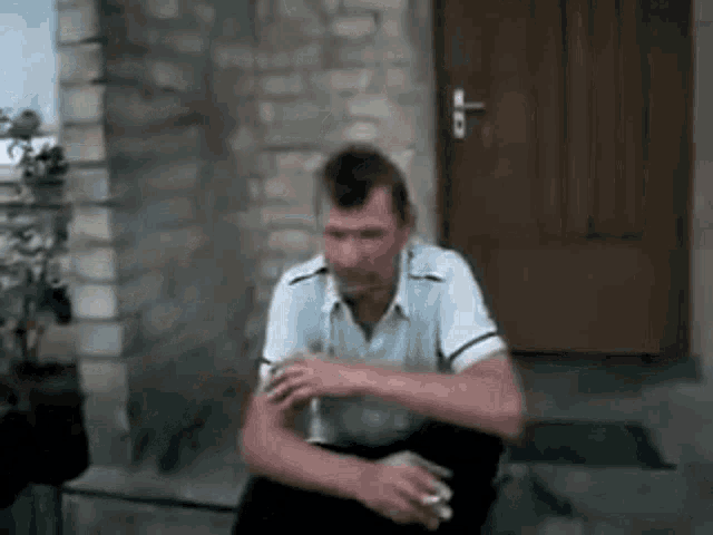 a man is sitting in front of a door smoking a cigarette and drinking a beer .