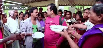 a man in a pink shirt is standing in front of a crowd of people holding plates .