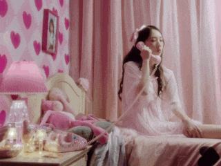 a girl is sitting on a bed talking on a telephone