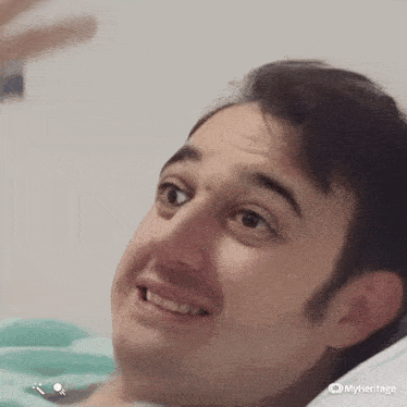a man is laying in a hospital bed smiling and looking up .