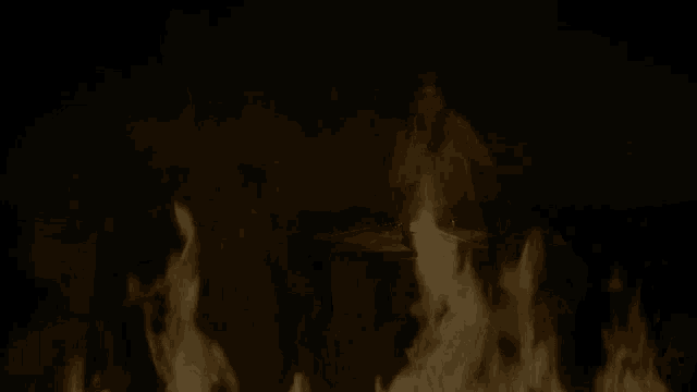 a woman is sitting at a table in front of a candle in a dark room surrounded by flames .