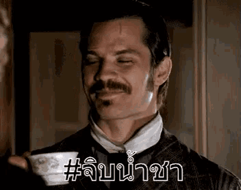 a man with a mustache is holding a cup of tea in his hand .