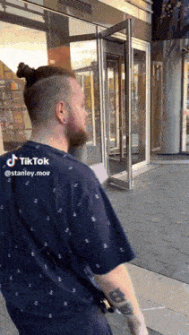 a man with a ponytail and a tattoo on his arm is standing in front of a building that says tiktok