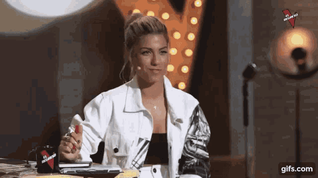 a woman in a white jacket is sitting at a table with a microphone and a cup that says " no love "