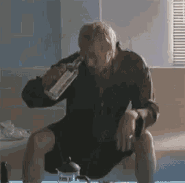 a man is sitting on a bed holding a bottle of alcohol .