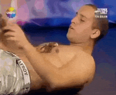 a shirtless man with a scorpion tattoo on his chest is laying on his stomach in front of a show sign