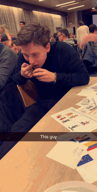 a man sits at a table eating a sandwich with a caption that says " this guy "