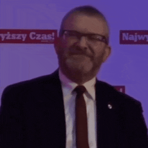 a man with a beard wearing glasses and a suit and tie is smiling .