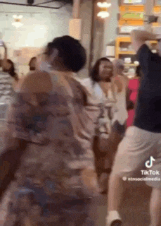 a group of people are dancing in a room while a woman takes a picture .
