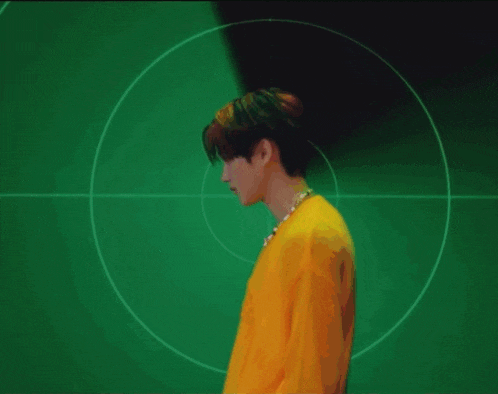 a man in a yellow shirt and necklace is standing in front of a green target .