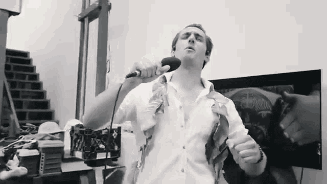 a black and white photo of a man singing into a microphone with a crate of coffee cups behind him