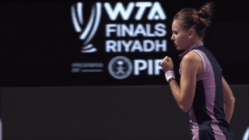 a woman is standing in front of a wta finals riyadh sign