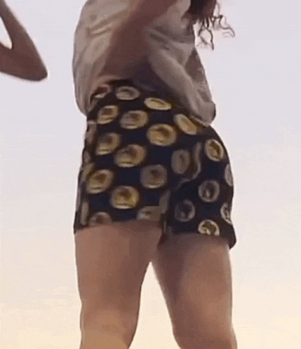 a woman is dancing on a beach wearing shorts with circles on them .