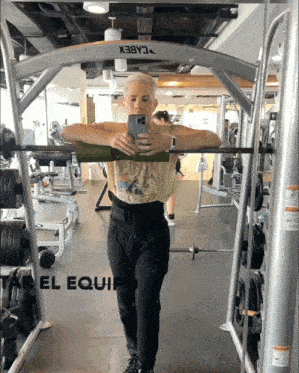 a woman taking a picture of herself in a gym with the word el equip on the bottom right