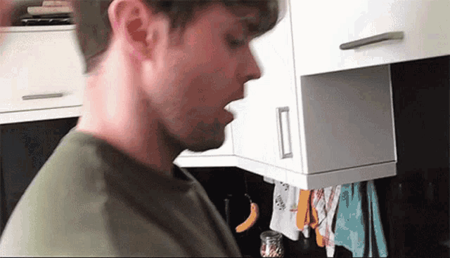 a man in a green shirt is standing in a kitchen eating a banana