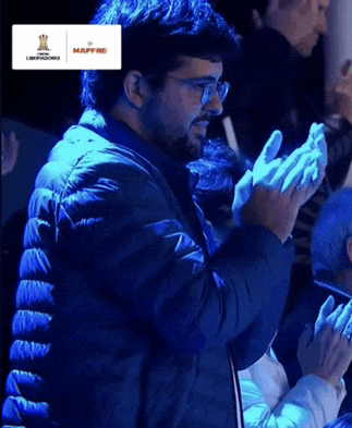 a man in a blue jacket is clapping his hands in a crowd