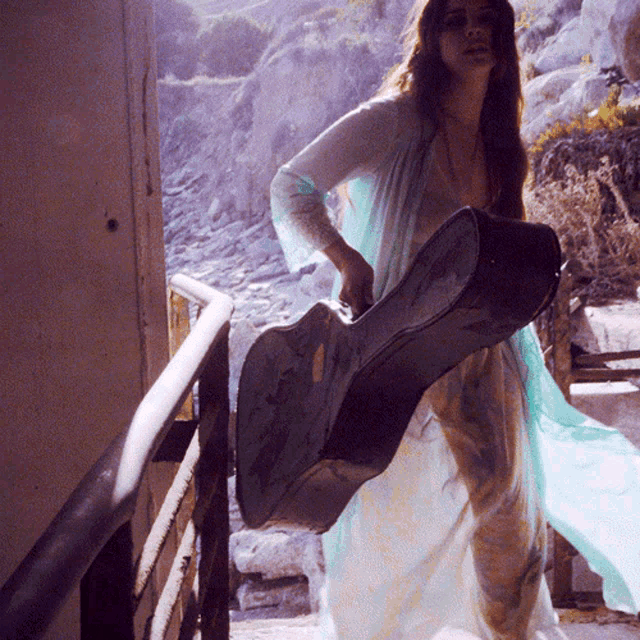 a woman in a white dress is carrying a black guitar case