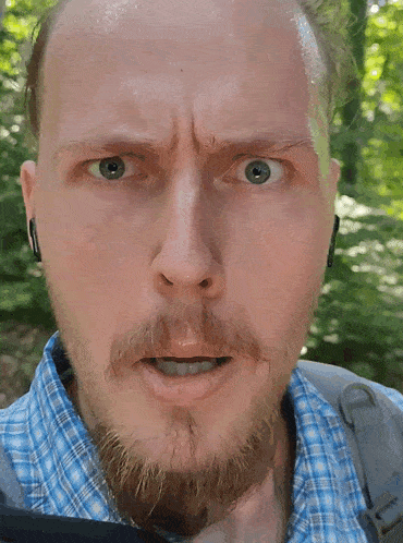 a man with a beard is wearing a blue plaid shirt and has a backpack on his back