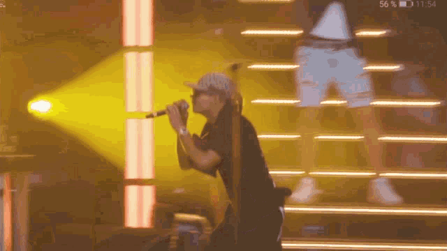 a man singing into a microphone with the time of 11:54 on the screen behind him
