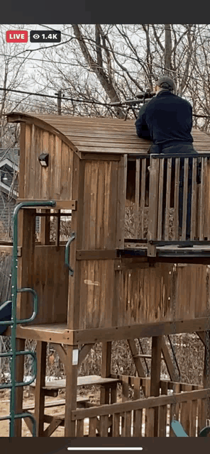 a man is standing on top of a wooden tree house with a sniper rifle