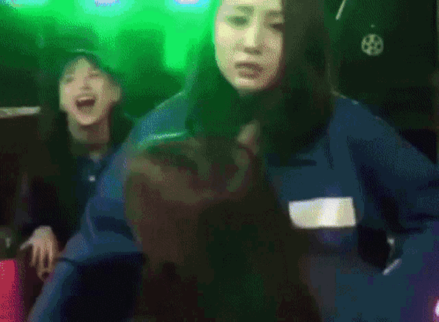 a woman in a blue jacket is dancing in a dark room with green lights behind her