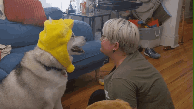 a woman wearing a green shirt with the word pee on it talks to a dog wearing a yellow hat