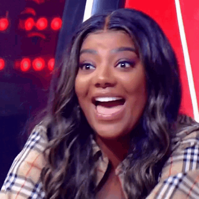 a woman in a plaid shirt is sitting in a chair with her mouth open and a surprised look on her face .