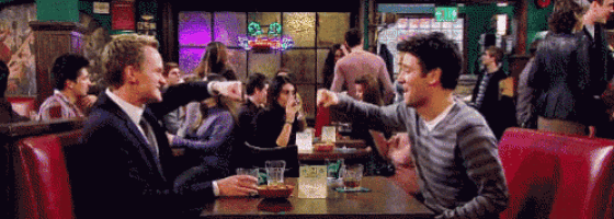 two men are sitting at a table in a restaurant and one of them is pointing at another man