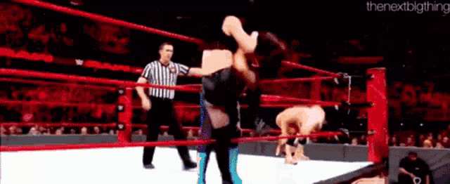 a wrestler is doing a handstand in a wrestling ring while a referee stands behind him .