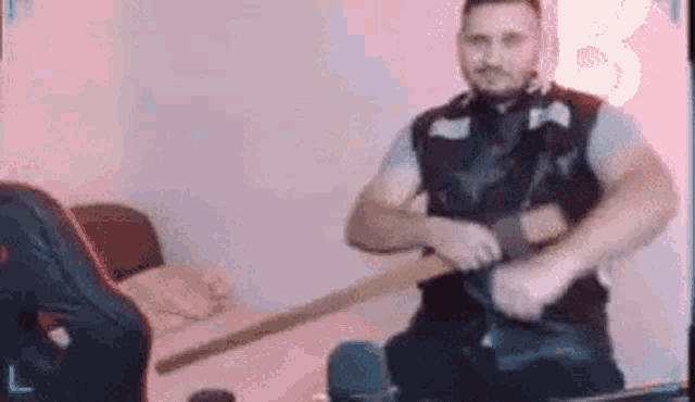 a man in a leather vest is holding a wooden stick in his hands .