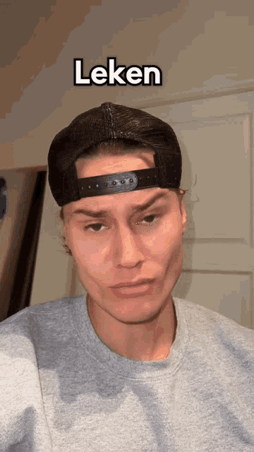 a man wearing a baseball cap and a grey shirt has the word " leken " above his head