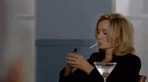 a woman is lighting a cigarette while sitting at a table with a martini glass .