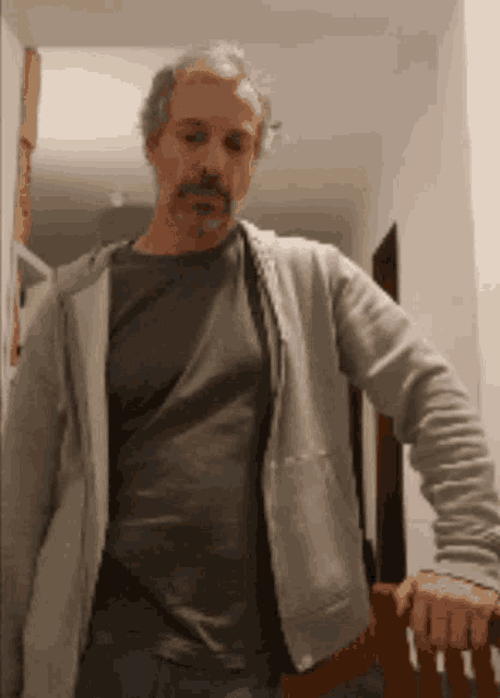 a man with a beard is standing in a hallway holding onto a chair