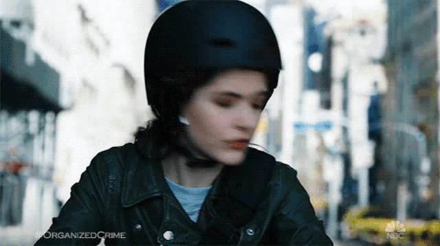 a woman wearing a black helmet and a leather jacket is riding a motorcycle .