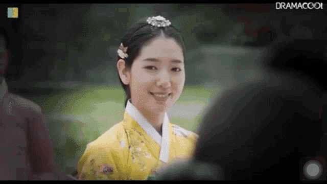 a woman in a yellow kimono is smiling and looking at someone .