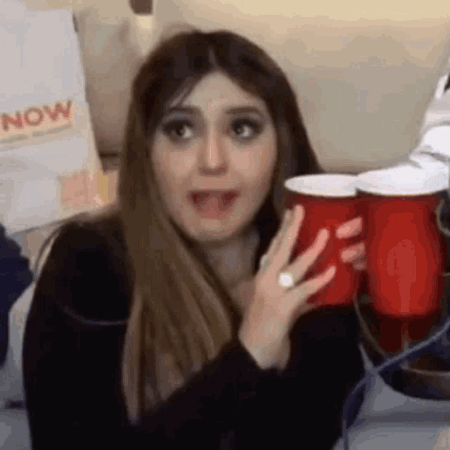 a woman is holding two red cups in her hand and making a face .