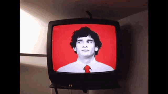 a man in a red shirt and tie is on a television screen