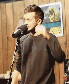 a man singing into a microphone in front of a wooden wall