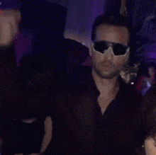a man wearing sunglasses and a black shirt is dancing in a dark room