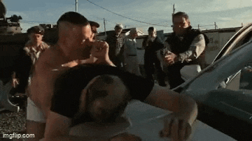 a group of men are standing around a car fighting each other .