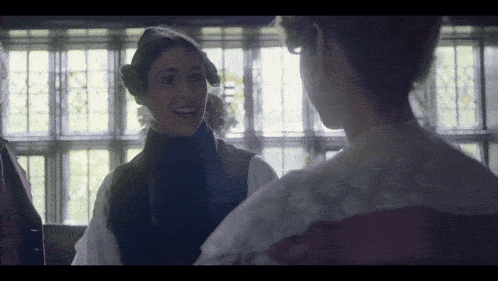 two women are standing next to each other in front of a window