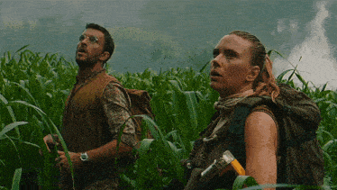 a man and a woman are standing in a field of tall grass and looking up